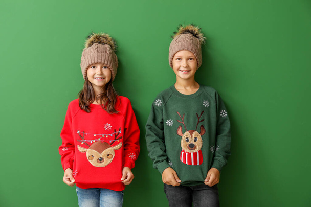 Niños pequeños en suéteres de Navidad y sombreros de punto sobre fondo de color
 - Foto, Imagen