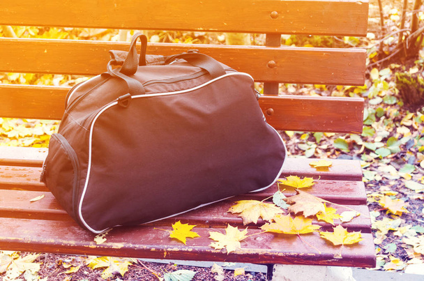 Traveling in autumn. Romantic time for a journey. A travel bag on a bench at bus stop in the country side. - Foto, Imagen