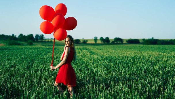 young woman posing with red balloons at sunny field - 写真・画像