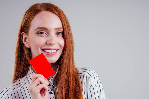 attractive redhead caucasian businesswoman wearing striped shirt holding credit card studio white background black friday sale :dentist stomatologist snow-white smile visiting card - Фото, зображення