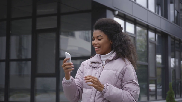 szczęśliwy Afryki amerykański kobieta biorąc selfie i wybierając zdjęcie w pobliżu budynku - Materiał filmowy, wideo