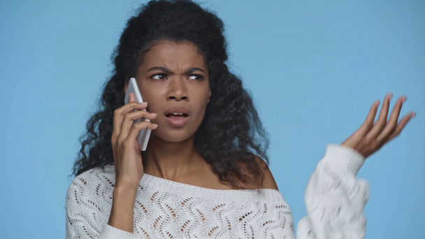disgustado mujer afroamericana enojado hablando en el teléfono inteligente y gesto aislado en azul
 - Imágenes, Vídeo