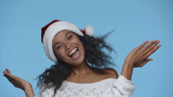 glücklich afrikanisch-amerikanische Frau mit Weihnachtsmannhut tanzt isoliert auf blau - Filmmaterial, Video