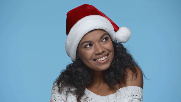 shy smiling african american woman in Santa hat flirting isolated on blue - Filmagem, Vídeo