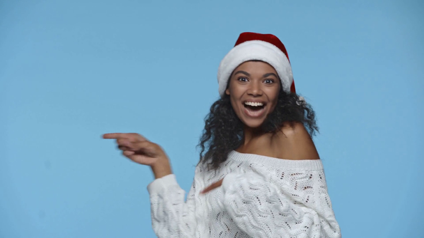 サンタの幸せなアフリカ系アメリカ人女性の帽子を指します指で青に隔離された - 映像、動画