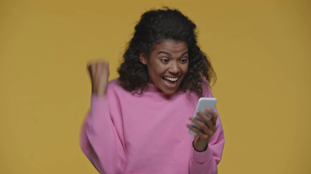 Mutlu Afro-Amerikan kızı akıllı telefon kullanıyor ve sarı renkte izole edilmiş bir jest gösteriyor. - Video, Çekim