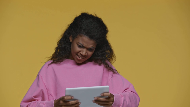 Χαρούμενη Αφροαμερικανή που παίζει βιντεοπαιχνίδι και δείχνει ψηφιακό tablet με λευκή οθόνη απομονωμένη στο κίτρινο - Πλάνα, βίντεο