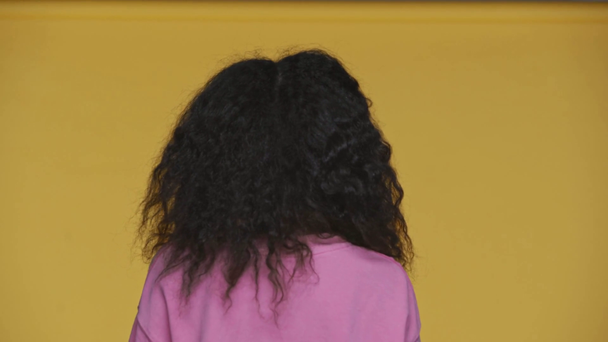 ピンクのスウェットシャツを着たアフリカ系アメリカ人の女の子は黄色で隔離され - 映像、動画
