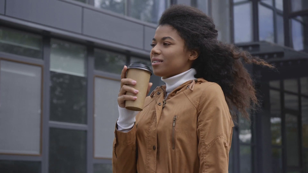 χαμογελαστή Αφροαμερικανή γυναίκα που περπατάει με καφέ για να βγει στο δρόμο - Πλάνα, βίντεο