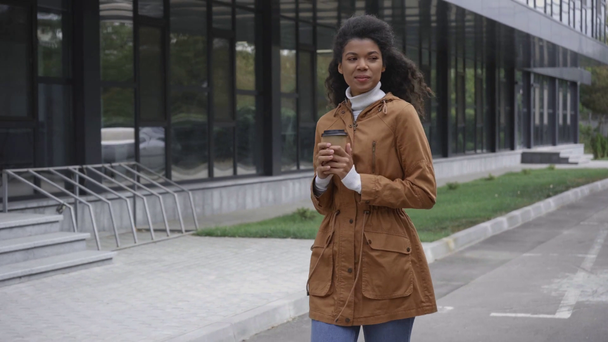 mujer afroamericana feliz caminando y bebiendo café de la taza de papel en la calle
 - Imágenes, Vídeo