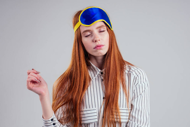 Good Morning. Smiling redhead young business woman in a striped shirt and blue yellow sleep mask white background studio - Photo, Image