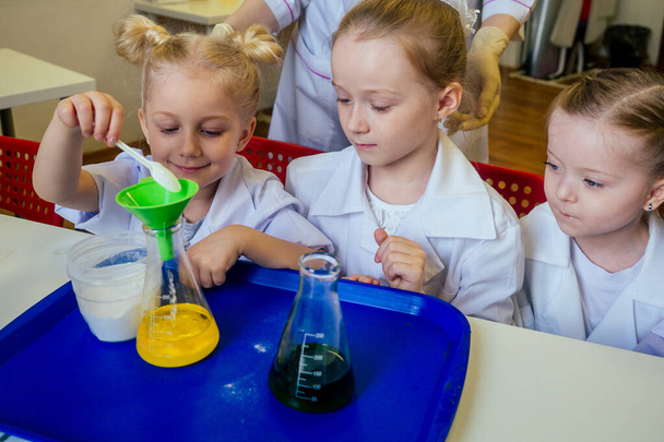 gruppo di scolarette con insegnante in laboratorio facendo esperimento osservando la reazione chimica con la tintura con aceto e soda vulcano indossando camice bianco vetro uniforme
 - Foto, immagini