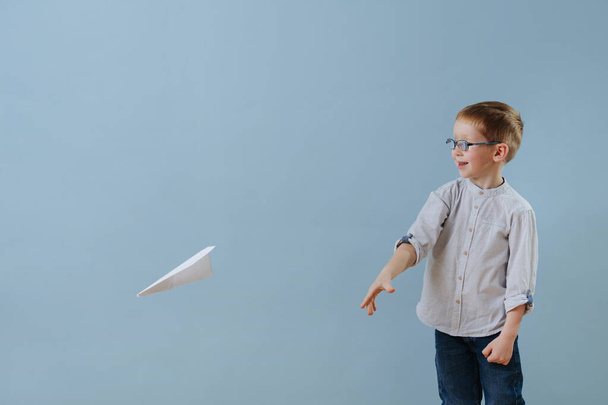 Lindo niño jengibre lanzó un avión de papel para volar sobre fondo azul
 - Foto, Imagen