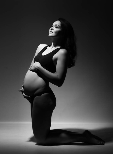Pregnant woman in a black bathing suit on a gray background. - Фото, зображення