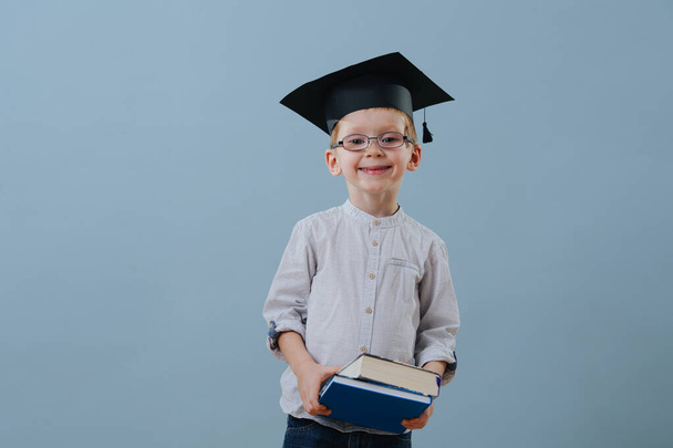 Redhead first grader boy in glasses, student hat holds stack of books in hands - Fotografie, Obrázek