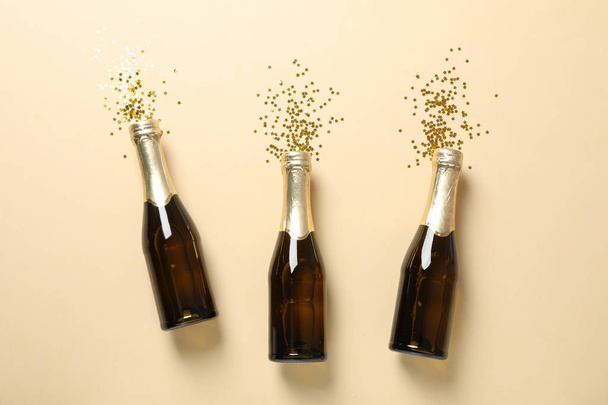 Champagne bottles and glitter on beige background, space for tex - Photo, Image