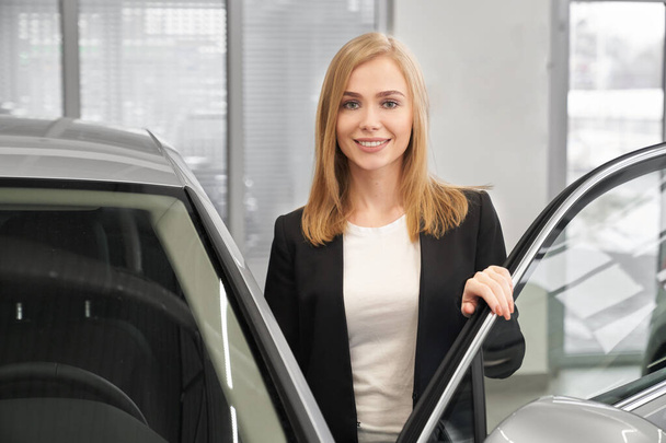 Front view of female client opening door of new car - Foto, Imagen