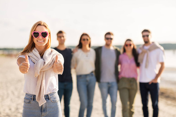 woman with friends on beach showing thumbs up - Foto, Bild