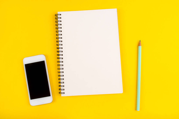 Empty notebook, pencil and phone on yellow background, top view. - Zdjęcie, obraz