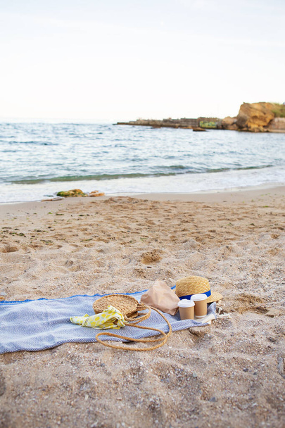 Голубая клетка, на которой пластиковые очки с кофе, сумка, шляпа на берегу моря
. - Фото, изображение