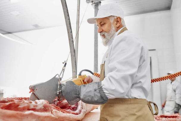 Butcher working with electric knife and cutting pork. - Zdjęcie, obraz