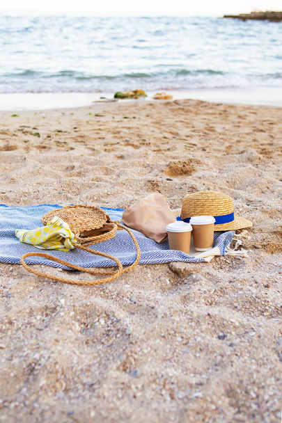 Un plaid bleu sur lequel se trouvent des verres en plastique avec café, un sac, un chapeau sur le bord de la mer
. - Photo, image