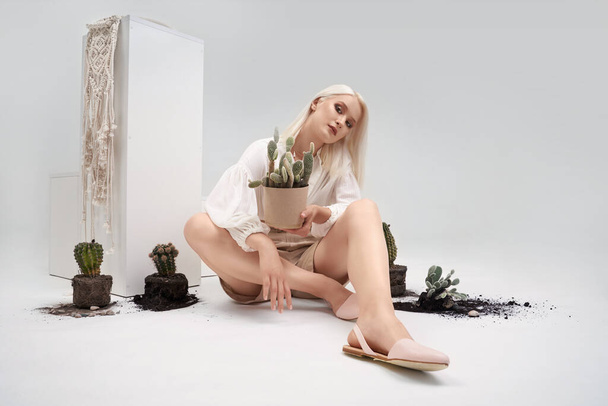 Attractive woman sitting on floor near pots with cactus - Foto, Imagen