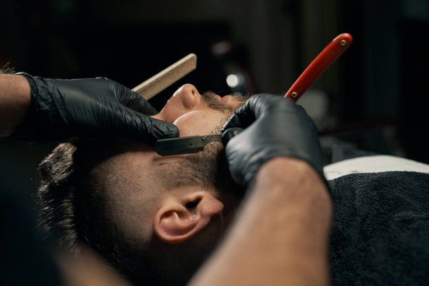 Handsome bearded man is getting shaved by hairdresser - Photo, Image