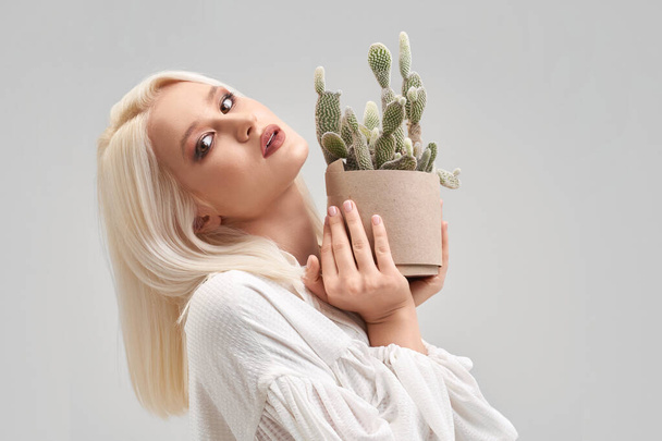 Beautiful blonde girl with make up holding pot with cactus - Фото, зображення