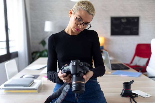 Modern young entrepreneur woman reviewing her last photographs in the camera while sitting in the office. - Foto, Bild