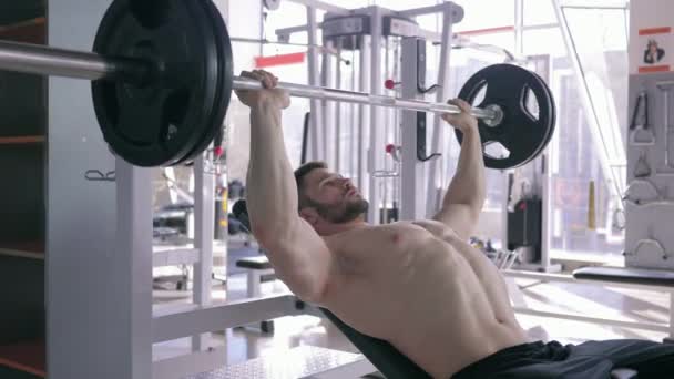 strong muscular sports male doing bench press with barbell while power working out in gym - Filmmaterial, Video