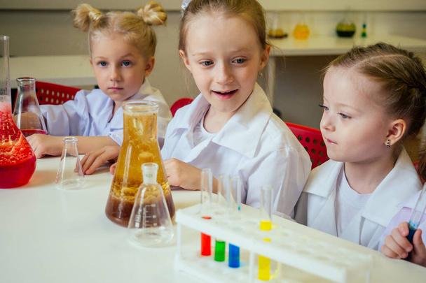 group of school girl kids with teacher in school laboratory making experiment observing the chemical reaction with the dye with vinegar and soda volcano wearing white gown uniform glass - Foto, Bild
