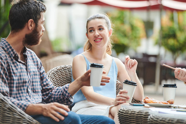 Mooie glimlachende jonge vrouw drinken van koffie en bespreken van plannen en ideeën met zakenpartners vergadering in outdoor cafe - Foto, afbeelding