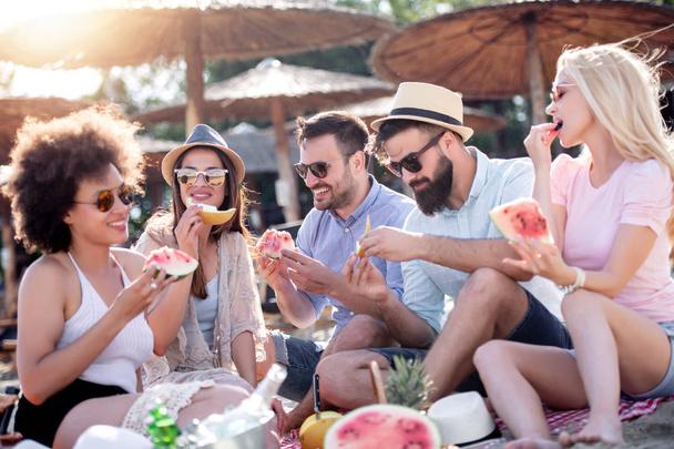 Vrienden die zich vermaken op het strand, watermeloen eten. - Foto, afbeelding