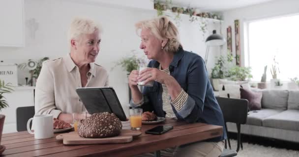 Mature lesbian couple looking at digital tablet at breakfast - Filmagem, Vídeo
