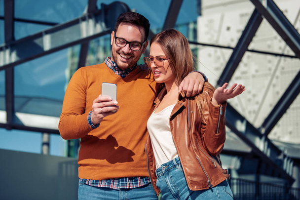 Young cheerful man and woman spending time together,using phone. - Foto, afbeelding