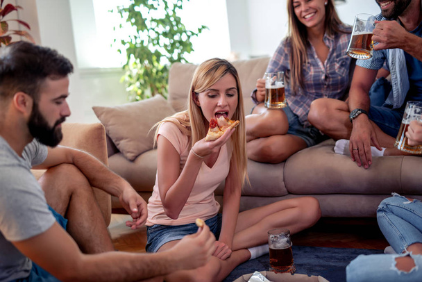Amici che si divertono insieme a casa, mangiano pizza e bevono birra
. - Foto, immagini