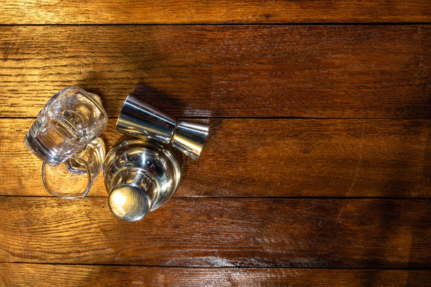 Cocktail shaker accessories and shots glasses on a wooden board. - 写真・画像