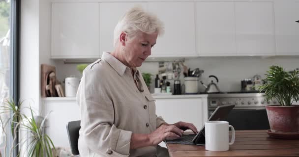 Mature adult woman in kitchen using a digital tablet with keypad - Imágenes, Vídeo
