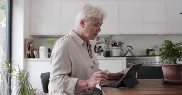 Mature adult woman in kitchen using a digital tablet with keypad - Filmagem, Vídeo