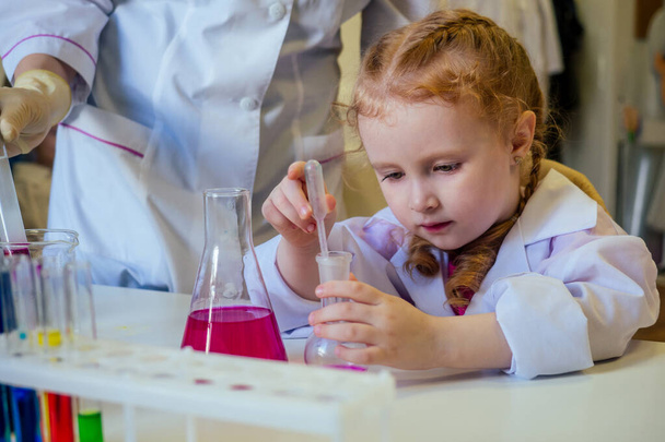 clever redhead school girl chemist in eyeglasses and white medical gown making science experiments chemistry ,mixing different chemical solutions in laboratory classroom - Fotó, kép