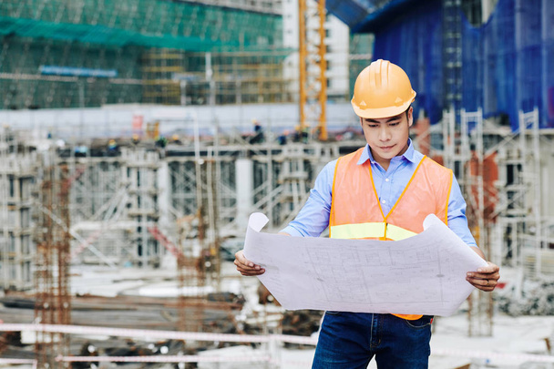 Engenheiro civil asiático profissional sério examinando o plano de construção na área de trabalho
 - Foto, Imagem