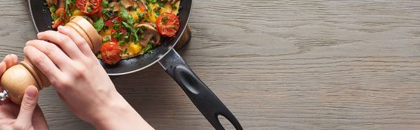 cropped view of woman sprinkling pepper on omelet with mushrooms, tomatoes and greens  - Foto, immagini