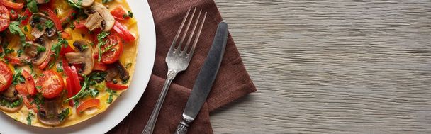 hausgemachtes Omelett mit Gemüse auf Holztisch mit Gabel, Messer und Serviette - Foto, Bild