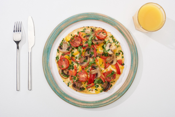 bovenaanzicht van smakelijke omelet voor ontbijt op witte tafel met sap, vork en mes - Foto, afbeelding