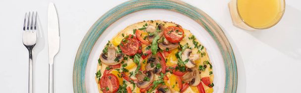 top view of plate with tasty omelet with tomatoes and mushrooms for breakfast on white table with juice, fork and knife - Photo, image