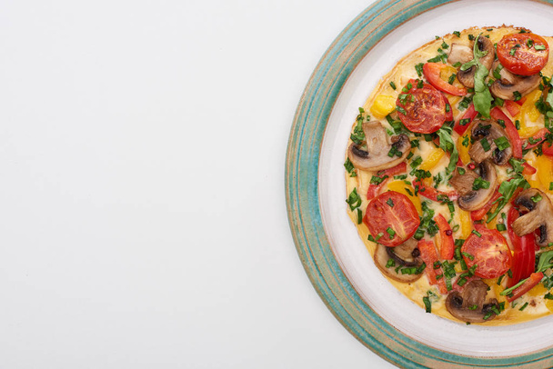 vista superior da placa com omelete saboroso com tomates, verdes e cogumelos para o café da manhã na mesa branca
  - Foto, Imagem