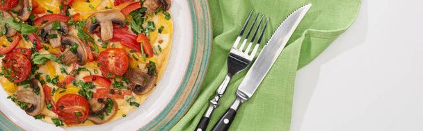 bovenaanzicht van zelfgemaakte omelet op bord met servet, vork en mes - Foto, afbeelding