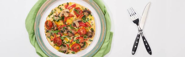 vrchní pohled na chutnou omeletu na talíři s ubrouskem, vidličkou a nožem - Fotografie, Obrázek