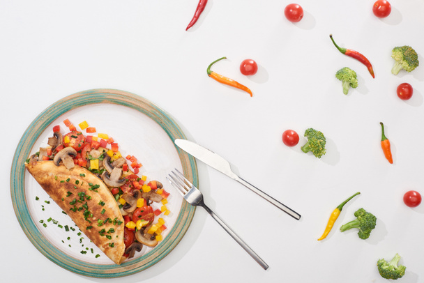 top view of plate with homemade wrapped omelet with vegetables on white table with chili peppers, tomatoes and broccoli - Фото, изображение
